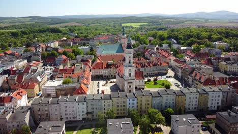 Prudnik-town-square,-showcases-the-historic-church-and-town-hall-amidst-red-roofed-buildings-and-lush-greenery