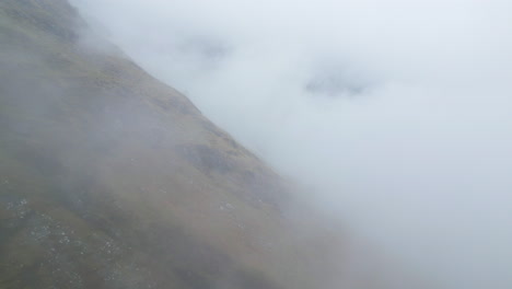 Aerial-flying-backwards-over-mountainside-in-dense-fog,-Glen-Coe,-Scotland