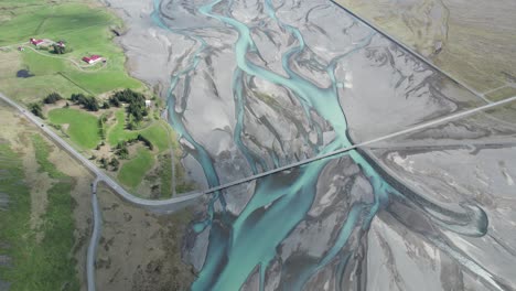 Aerial-view-of-a-bridge-crossing-a-blue-glacier-river-on-the-Ring-Road-in-Iceland-during-summer,-highlighting-the-vibrant-river-hues-and-surrounding-landscapes