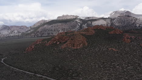 Snow-capped-mountains-with-rugged-red-hills-in-the-foreground,-and-diverse-landscape-of-the-Eastern-Sierra