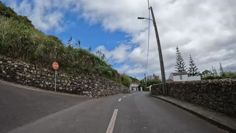 Driving-on-a-winding-road-in-Sao-Miguel,-Azores,-with-a-red-car-approaching-a-stop-sign