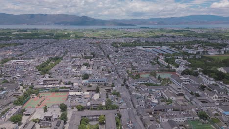 Drone-footage-of-the-main-pedestrian-street-of-Dali's-Ancient-City,-with-the-magnificent-Er-Hai-and-Mountains-in-the-backdrop