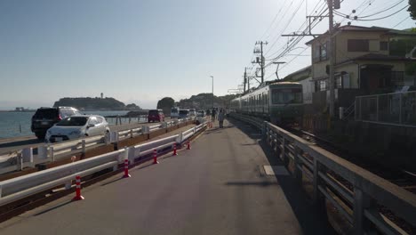 POV-walking-next-to-Enoden-train-driving-through-Kamakura-with-Enoshima-in-distance