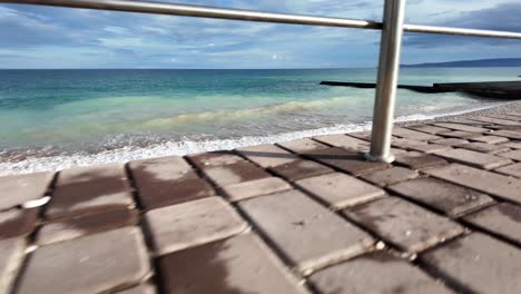 A-relaxing-view-of-waves-gently-crashing-on-a-pebbled-shore,-framed-by-a-metal-railing