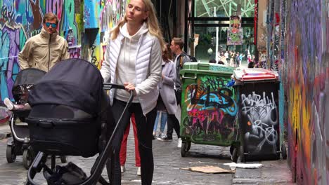 Turistas-Que-Visitan-Hosier-Lane-En-La-Ciudad-De-Melbourne,-Una-Famosa-Calle-Adoquinada-Que-Muestra-Una-Vibrante-Variedad-De-Murales-Artísticos-Y-Graffiti-En-Las-Paredes-Exteriores-De-Los-Edificios-Y-Los-Icónicos-Contenedores-Con-Ruedas-Australianos.