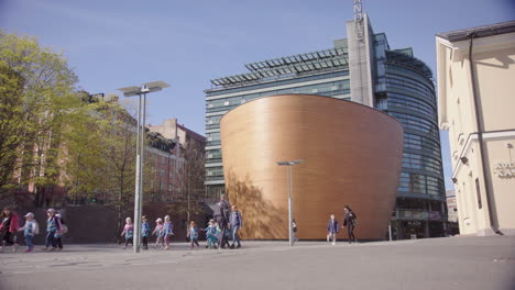 Un-Grupo-Escolar-Joven-Pasa-Por-La-Contemporánea-Capilla-Kamppi-De-Madera-Curvada-En-Helsinki.