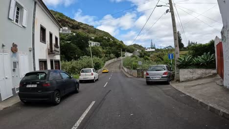 POV-driving-through-a-quiet-village-on-Sao-Miguel-island,-Azores-with-lush-greenery-and-cloudy-sky