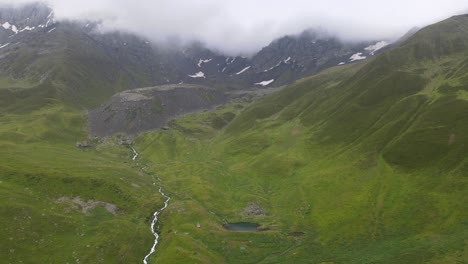 drone-shot-of-lake-and-river-in-the-middle-of-mountains-with-cloud-and-fog-in-the-background-caucasian-mountains