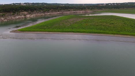 Aerial-shot-of-small-island-with-green-grass-surrounded-by-calm-water-at-Canyon-Lake-in-Texas