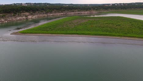 Toma-Aérea-De-Una-Pequeña-Isla-Con-Hierba-Verde-Rodeada-De-Aguas-Tranquilas-En-El-Lago-Canyon-En-Texas