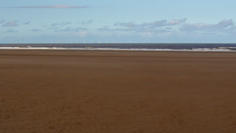 extra-wide-shot-of-waves-breaking-onto-a-flat-sandy-beach-at-Saltfleet,-Louth,-Lincolnshire