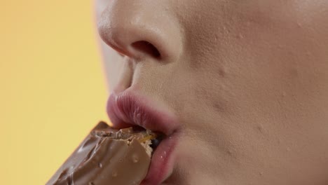 woman-taking-a-bite-of-a-chocolate-bar,-close-up-biting-of-snack-on-yellow-background