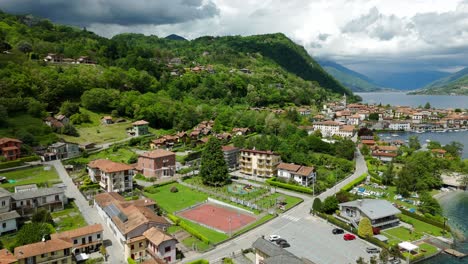 Una-Toma-Aérea-Captura-Una-Pintoresca-Ciudad-Ubicada-Junto-A-Un-Lago-Con-Exuberante-Vegetación-Y-Nubes-En-Lo-Alto