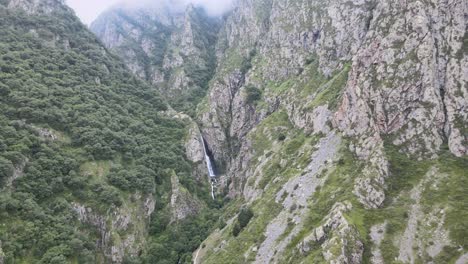 drone-shot-of-waterfall-in-the-middle-of-caucasian-mountains-with-rocks-clouds-and-green-trees-and-fog