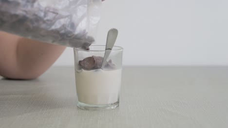 Person-pouring-chocolate-cereal-into-a-glass-of-milk