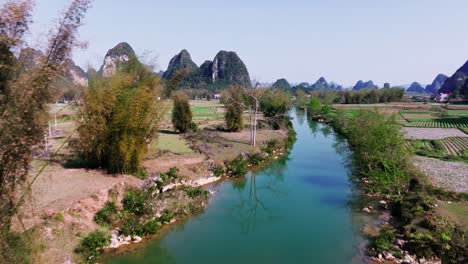 The-drone-flies-over-a-picturesque-river,-lush-rice-fields,-stunning-limestone-mountains-that-characterize-the-landscape,-vibrant-greenery-and-the-peaceful-ambiance-of-this-rural-area