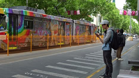 Tram-running-across-Swanston-street,-commuters-waiting-at-the-tram-stop,-tourists-touring-the-city-with-electric-bikes,-in-the-heart-of-Melbourne's-bustling-central-business-district