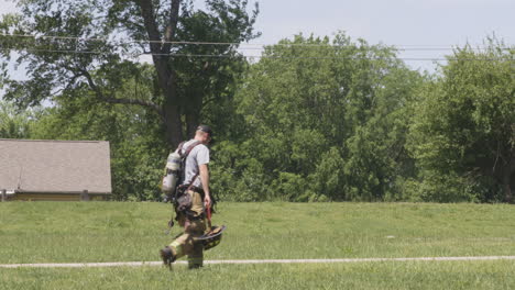 Fireman-With-Fire-Extinguisher-And-Safety-Helmet-Walking-On-Field-During-Firefighting-Exercise-In-Siloam-Springs,-Arkansas