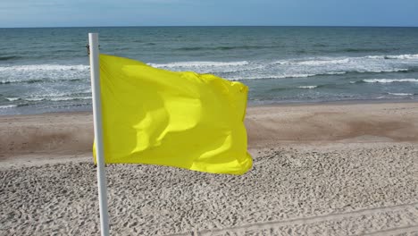 Yellow-flag-flying-on-beach,-aerial,-drone-shot