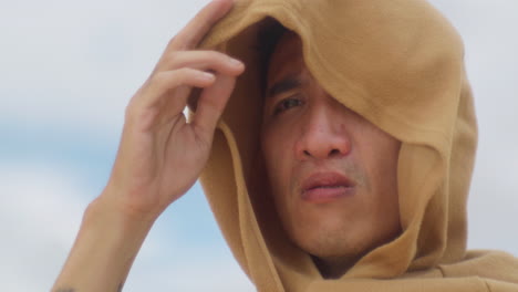 close-up-of-a-male-chinese-asiatic-wearing-a-robe-hood-looking-at-the-distance-with-a-worried-gaze-during-a-wind-storm