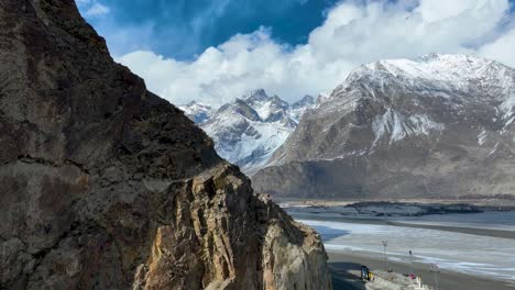 Areial-breathtaking-view-of-towering-mountains-under-a-blue-sky-with-clouds,-featuring-rocky-terrains-and-a-valley