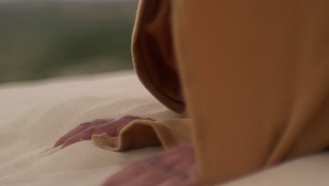 close-up-of-man-wearing-a-robe-falling-on-desert-sand-on-his-hands