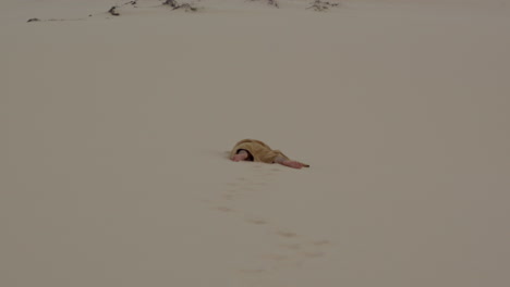 death-monk-male-man-in-robe-laid-on-the-ground-at-distance-in-desert-sand-dunes