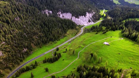 Toma-Aérea-De-Un-Valle-Verde-Con-Una-Carretera-De-Montaña-En-Suiza