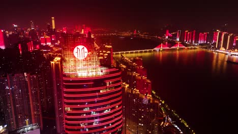 Orbit-night-view-of-a-commercial-building-with-lake-and-Sanchaji-bridge-at-the-background-at-Changsha-City,-Hunan,-China