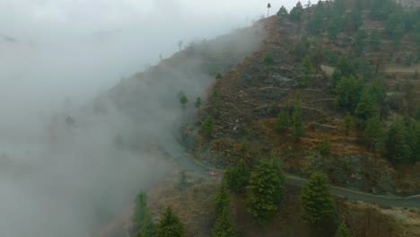 Luftaufnahme-Eines-Nebligen-Berghangs-Mit-Einer-Gewundenen-Straße,-Deren-Nebel-Die-Bäume-Und-Die-Landschaft-Einhüllt