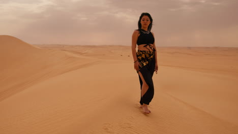 Barefoot-Asian-woman-in-traditional-attire-standing-on-a-dune-in-the-desert