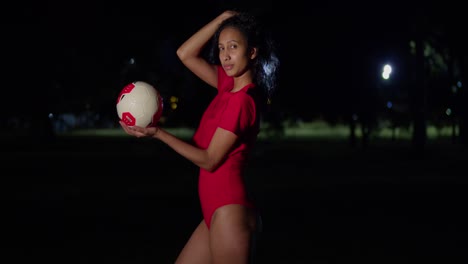 Por-La-Noche,-Una-Joven-Vestida-En-Bikini-Tiene-Una-Pelota-De-Fútbol-En-La-Mano.