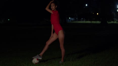 With-a-football-in-her-hand,-a-young-girl-in-a-bikini-stands-in-the-night