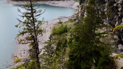 Aerial-take-of-The-Oeschinen-blue-lake-in-Switzerland,-surrounded-by-trees-and-rocky-walls