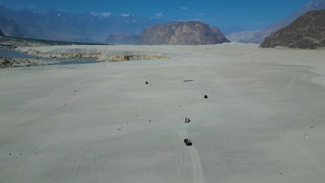 High-angle-drone-shot-of-mountain-terrain-vehicles-driving-on-Sarfaranga-Cold-Desert-in-Skardu-valley,-Pakistan