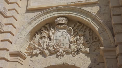 Coat-of-arms-above-an-arched-entry-in-the-ancient-part-of-Mdina,-the-old-capital-of-Malta