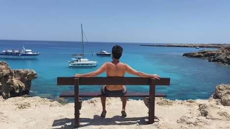 Man-sitting-alone-on-the-bench-by-the-lagoon-looking-out-at-the-boats