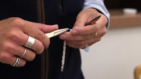 Jeweller-standing-in-shop-using-pliers-to-make-silver-bracelet-for-selling