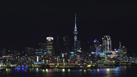 Auckland-New-Zealand-Sky-Tower,-skyline,-with-lights-reflecting-off-the-water---pullback-reveal