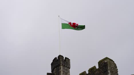 Welsh-flag-flying-on-a-castle-tower-in-slow-motion,-view-against-overcast-sky