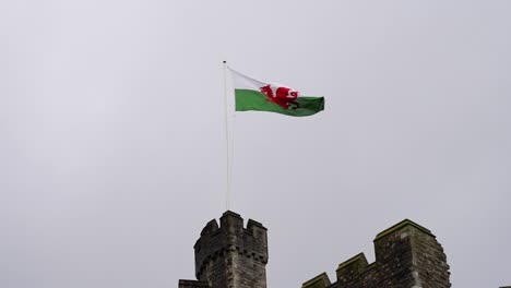 Bandera-Galesa-Ondeando-En-La-Torre-De-Un-Castillo-En-Cámara-Lenta,-Vista-Contra-El-Cielo-Nublado