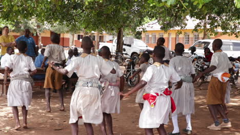 Niños-Y-Niñas-Negros-Africanos-Estudiantes-Vestidos-De-Uniforme-Realizando-Juntos-Una-Danza-Tribal-Tradicional-En-Una-Remota-Aldea-Rural