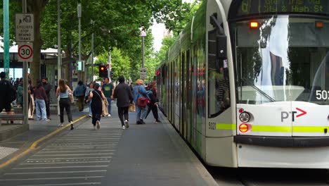 Passengers-disembarking-and-boarding-the-tram-at-the-stop-in-front-of-State-Library-Victoria-along-Swanston-street,-in-the-bustling-Melbourne-central-business-district