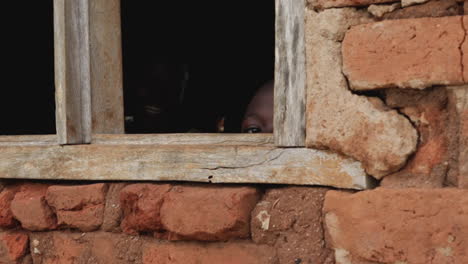 Niño-Africano-Mirando-A-Través-De-Una-Ventana-De-Ladrillo-Rústico-En-Kampala,-Uganda