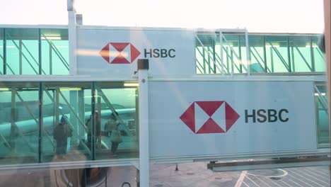 Flight-passengers-walk-through-a-plane-boarding-tunnel-decorated-with-the-logo-of-HSBC,-a-British-banking-and-financial-services-company,-at-Dubai-International-Airport,-United-Arab-Emirates-