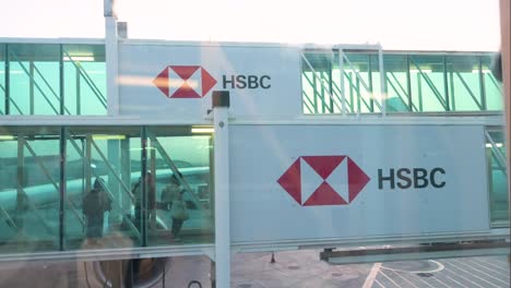 Los-Pasajeros-Del-Vuelo-Caminan-Por-Un-Túnel-De-Embarque-Decorado-Con-El-Logotipo-De-HSBC,-Una-Empresa-Británica-De-Servicios-Bancarios-Y-Financieros,-En-El-Aeropuerto-Internacional-De-Dubai,-Emiratos-Árabes-Unidos.-