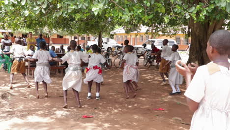 Children-dancing-in-a-schoolyard-in-Kampala,-Uganda-under-large-green-trees
