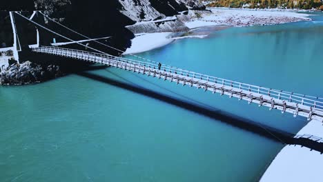 Backward-drone-view-of-a-bridge-over-water-flowing-lake-in-Skardu-Valley,-Pakistan