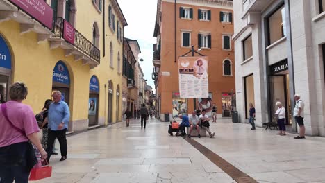 People-walking-over-small-square-in-Verona-with-colourful-facades,-small-shops,-and-shiny-tiled-floor