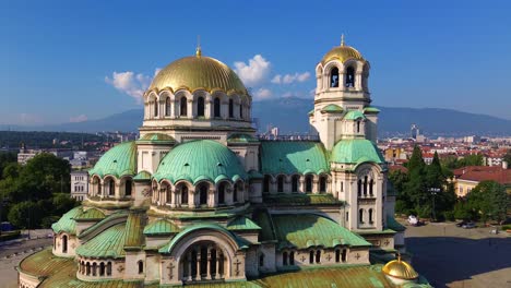 Epic-rising-shot-of-a-majestic-cathedral,-reveals-a-massive-cityscape-with-a-mountain-in-the-background-on-a-summer-day-with-clear-sky